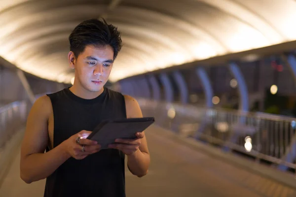 Πορτρέτο του όμορφος Ασίας νεαρός χρησιμοποιώντας ψηφιακό tablet σε εξωτερικούς χώρους, τη νύχτα — Φωτογραφία Αρχείου