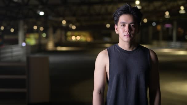 Retrato de joven feliz guapo asiático con los brazos cruzados al aire libre en la noche — Vídeos de Stock