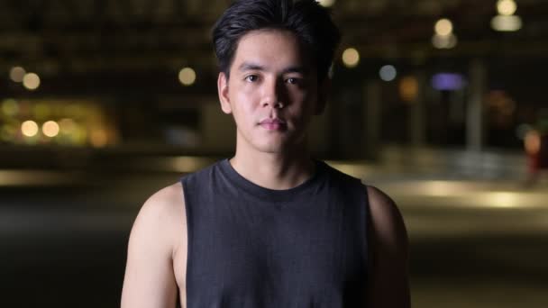Porträtt av ung glad Vacker asiatisk man ler utomhus på natten — Stockvideo