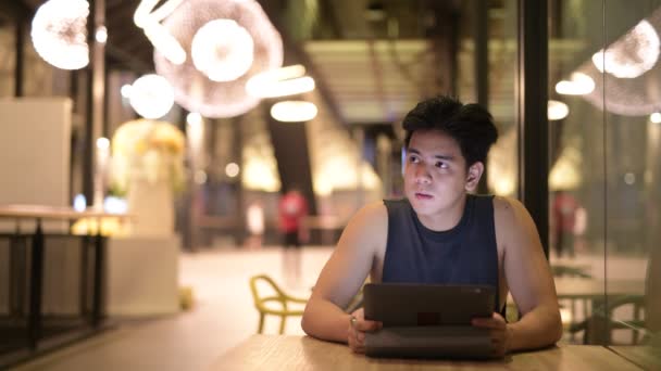 Gelukkig knappe Aziatische jongeman met behulp van digitale tablet in het restaurant bij nacht — Stockvideo