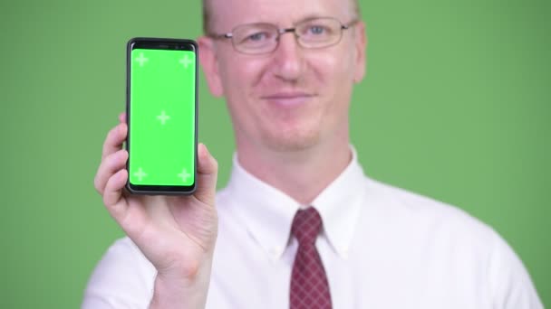 Happy mature bald businessman showing phone — Stock Video