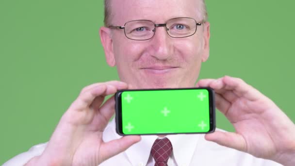 Щасливий зрілий лисий бізнесмен посміхається, показуючи телефон — стокове відео