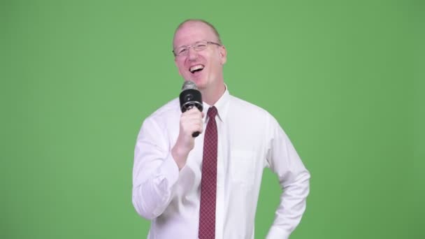 Happy mature bald businessman singing on the microphone — Stock Video