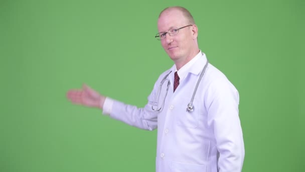 Счастливый взрослый лысый врач показывает что-то на зеленом фоне — стоковое видео