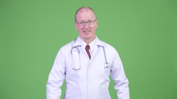 Feliz hombre calvo maduro médico pensando mientras que da pulgares hacia arriba — Vídeo de stock