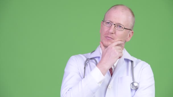 Happy mature bald man doctor smiling while thinking — Stock Video