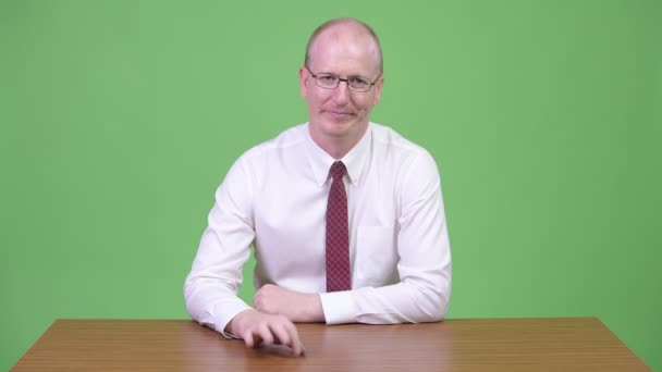 Mature bald businessman looking bored against wooden table — Stock Video