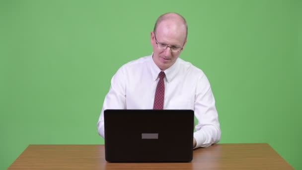 Angry mature bald businessman talking to the laptop against wooden table — Stock Video