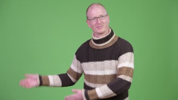 Happy ώριμος άνδρας φαλακρός με ζιβάγκο πουλόβερ δείχνει κάτι — Αρχείο Βίντεο