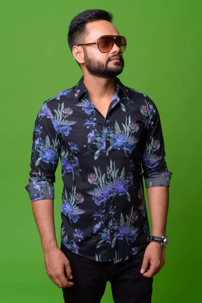 Young bearded Indian man against green background