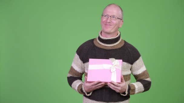 Happy mature bald man thinking while holding gift box — Stock Video