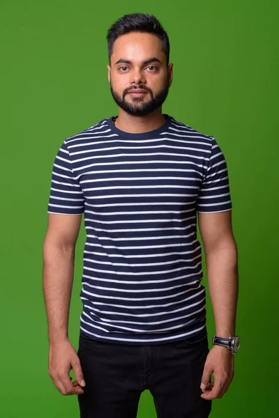 Young bearded Indian man against green background