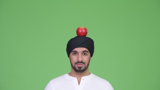 Ung förvånad skäggig indisk man bär turban med apple ovanpå huvudet — Stockvideo