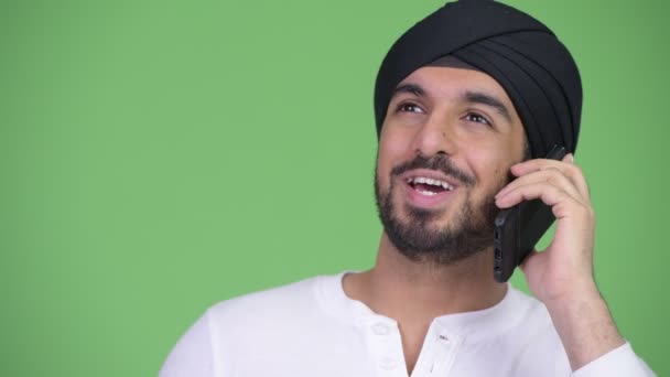 Молодой счастливый бородатый индиец думает, разговаривая по телефону — стоковое видео