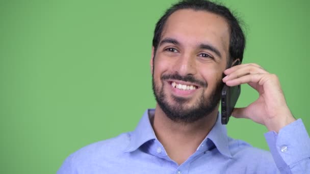 Jonge gelukkig bebaarde Indiase zakenman die denken tijdens het gesprek op de telefoon — Stockvideo