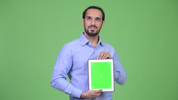 Young happy bearded Indian businessman thinking while showing digital tablet — Stock Video