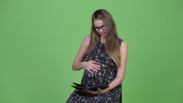 Jeune femme enceinte heureuse livre de lecture — Video