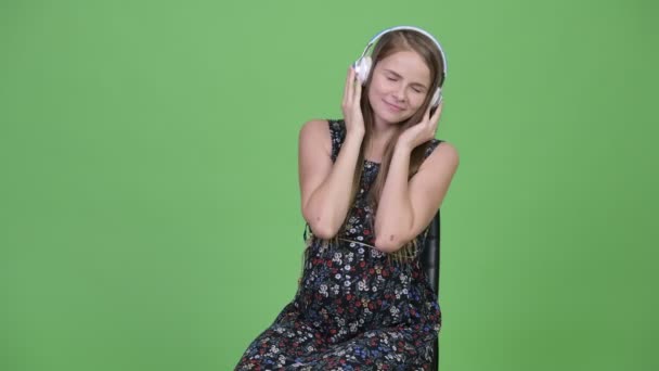 Молодая счастливая беременная женщина сидит, слушая музыку — стоковое видео