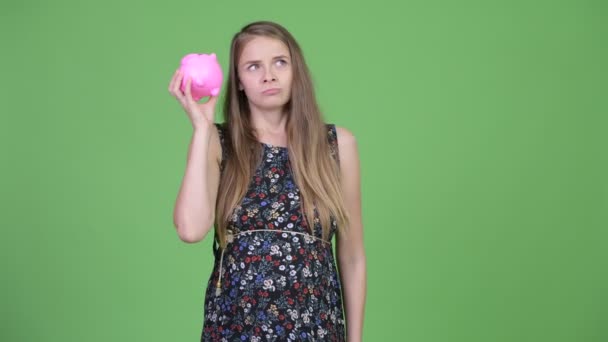 Junge schöne schwangere Frau schüttelt Sparschwein — Stockvideo