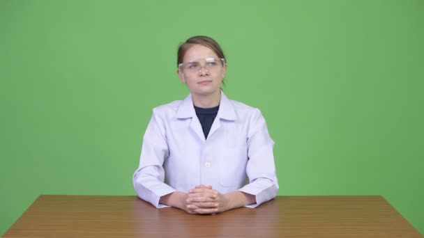 Jovem mulher bonita médico vestindo óculos de proteção enquanto pensa — Vídeo de Stock