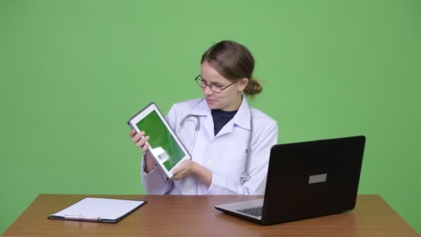 Jovem mulher bonita médico vídeo chamando com laptop contra mesa de madeira — Vídeo de Stock