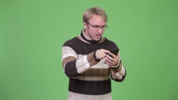 Studio πλάνο ξανθιά όμορφος άνδρας, χρησιμοποιώντας το τηλέφωνο και να αναζητούν σοκαρισμένος — Αρχείο Βίντεο