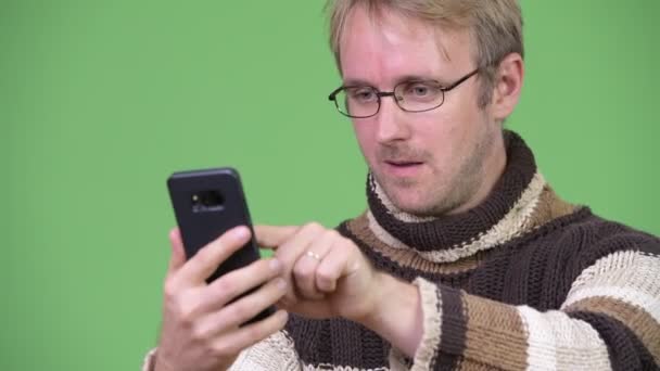 Studioaufnahme eines glücklichen gutaussehenden Mannes, der sein Handy benutzt und überrascht aussieht — Stockvideo