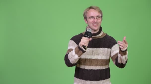 Студійний знімок блондинки красивий чоловік використовує мікрофон і виглядає винним — стокове відео
