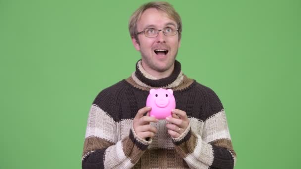 Studio shot van gelukkig knap man denken terwijl piggy bank — Stockvideo