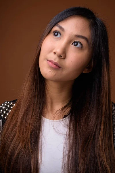 Jonge mooie Aziatische vrouw tegen bruine achtergrond — Stockfoto