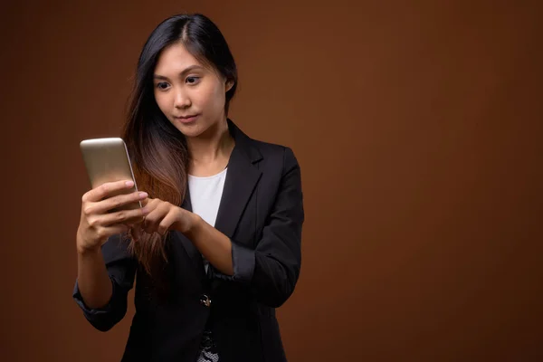 Young beautiful Asian businesswoman against brown background — Stock Photo, Image