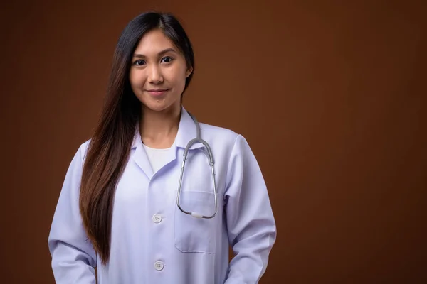Jovem bela mulher asiática médico contra fundo marrom — Fotografia de Stock