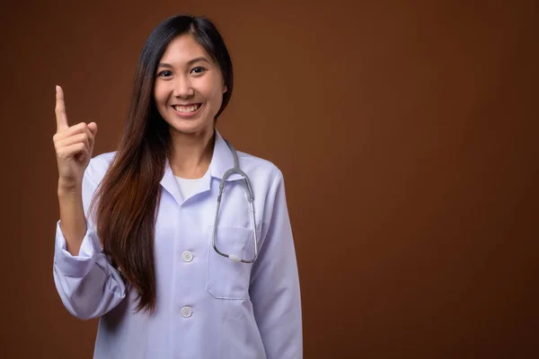 Молодая красивая азиатка врач на коричневом фоне — стоковое фото