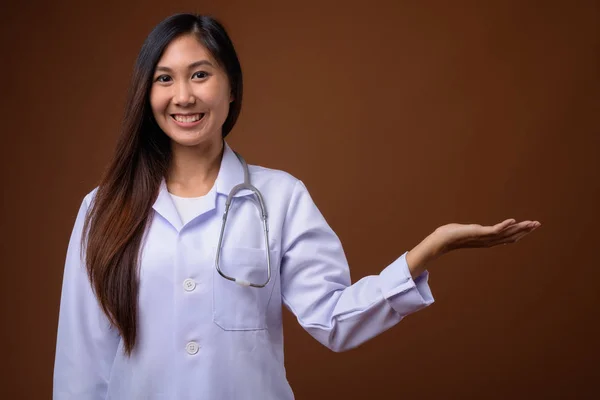 Молодая красивая азиатка врач на коричневом фоне — стоковое фото