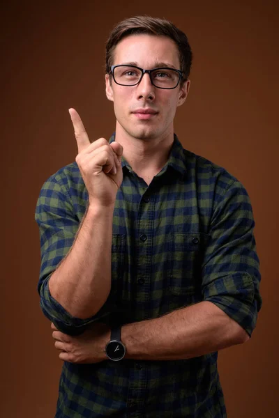 Ung vacker man bär glasögon mot brun bakgrund — Stockfoto