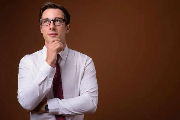 Joven hombre de negocios guapo usando anteojos contra la espalda marrón — Foto de Stock