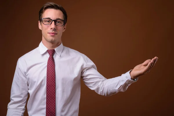 Jonge knappe zakenman dragen van bril tegen bruine rug — Stockfoto