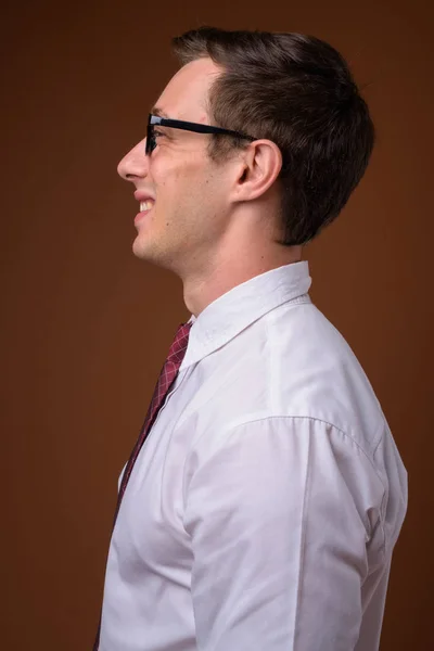 Jovem empresário bonito vestindo óculos contra costas castanhas — Fotografia de Stock