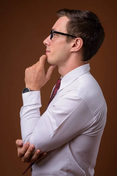 Młody przystojny biznesmen noszenie okularów przeciwko brązowy grzbiet — Zdjęcie stockowe