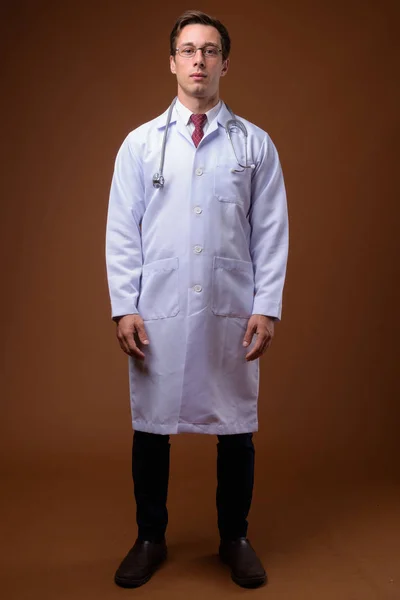 Young handsome man doctor against brown background — Stock Photo, Image