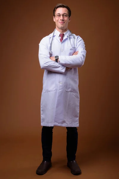 Young handsome man doctor against brown background — Stock Photo, Image