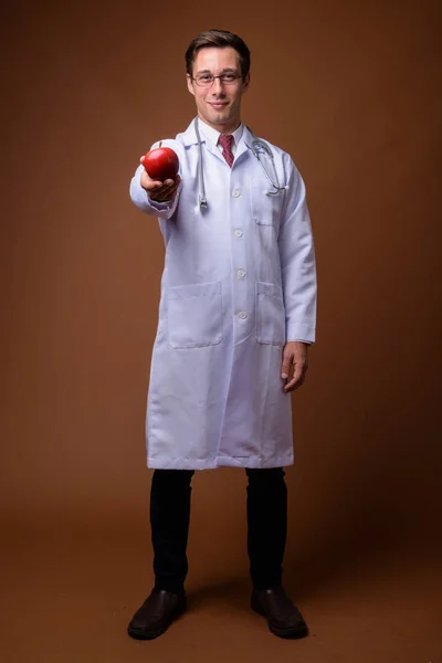 Молодой красивый мужчина врач на коричневом фоне — стоковое фото