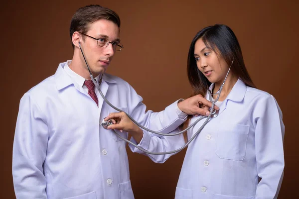 Estudio de dos médicos jóvenes juntos contra el fondo marrón —  Fotos de Stock