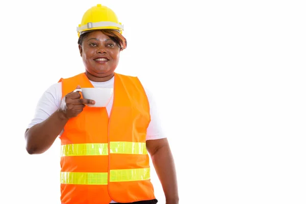 幸せな脂肪黒アフリカの女性建設労働者のスタジオショット笑顔とコーヒーカップを保持しながら考えて — ストック写真