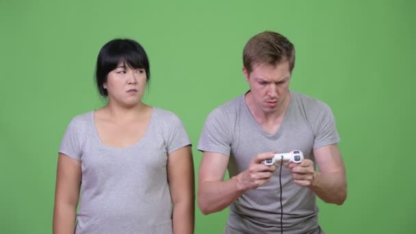 Young man playing games while overweight Asian woman looking upset — Stock Video