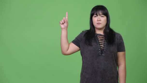 Feliz sobrepeso mujer asiática pensando mientras señala el dedo hacia arriba — Vídeos de Stock