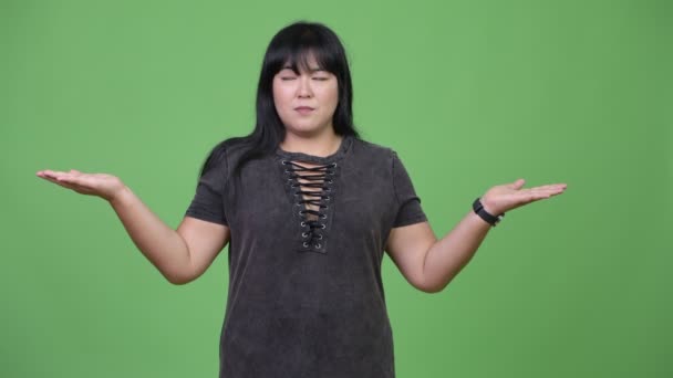 Schöne übergewichtige asiatische Frau vergleicht etwas — Stockvideo