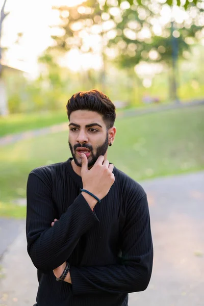 Young handsome Indian man thinking with hand on lip on the side