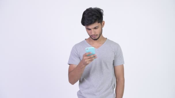 Joven hombre indio barbudo feliz usando el teléfono y recibiendo buenas noticias — Vídeos de Stock