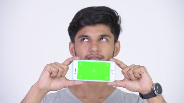 Young gelukkig bebaarde Indier denken terwijl het tonen van de telefoon — Stockvideo